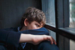 teen boy sits near a window showing some anxiety symptoms in teens