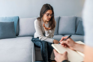a teen girl sits on a couch talking to her doctor while participating in psychotherapy for depression