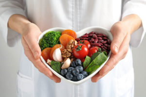 a photo of a person holding a heart-shaped dish full of fruits and vegetables talking about how diet and mental health are linked