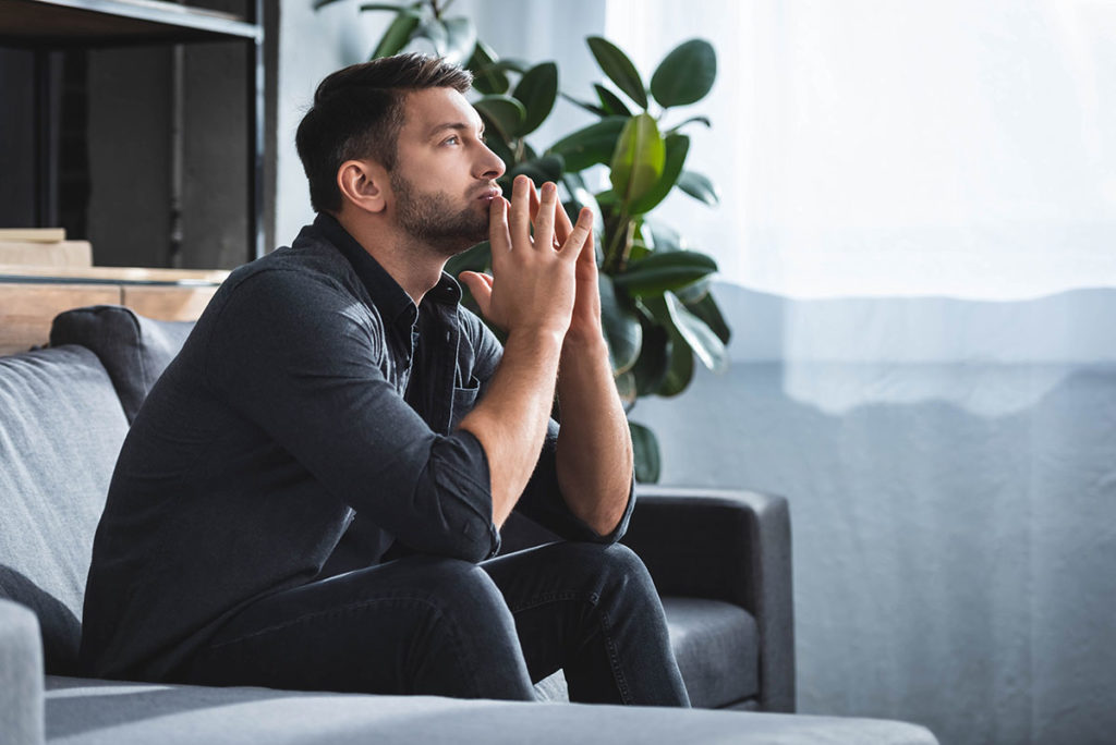 a man sits on a couch appearing to be distraught about how alcohol and anxiety are linked