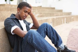 a teen boy sits outside on steps thinking about the long term effects of trauma