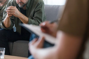 a photo of an out of focus person making notes on clipboard while another person sits on the couch during their anger management program