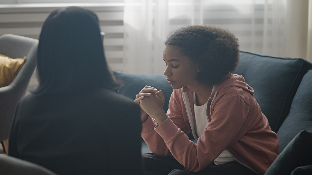 a young girl sits on a couch talking addressing trauma with her therapist