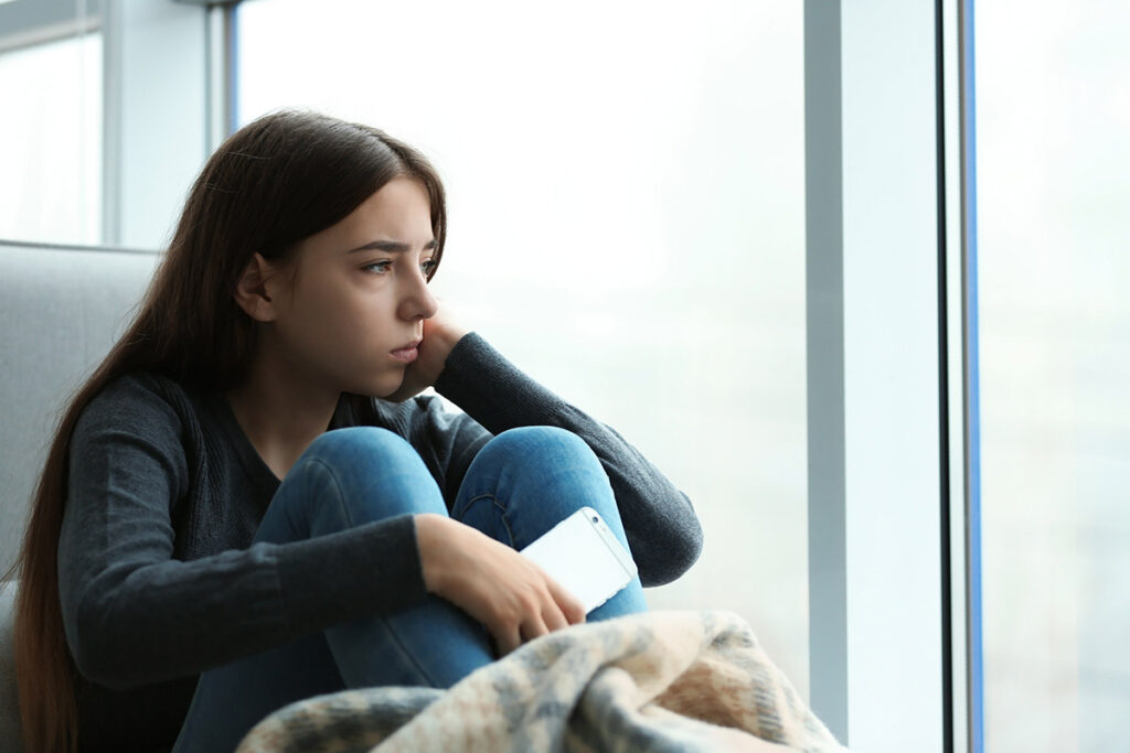 a distraught teen girl sits near a window while at outpatient treatment for anxiety and looks out the window