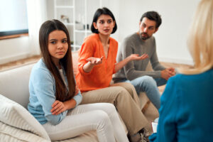 family of three sit on a couch together while the mother talks during family programming