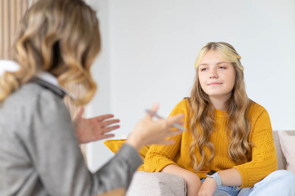 a teen girl sits on a couch and listens to therapist talking during the teen's cognitive-behavioral therapy for teens