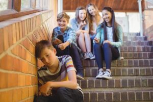 a group of young people sit on a set of stairs and bully the kid in front of them who is enduring the effects of bullying
