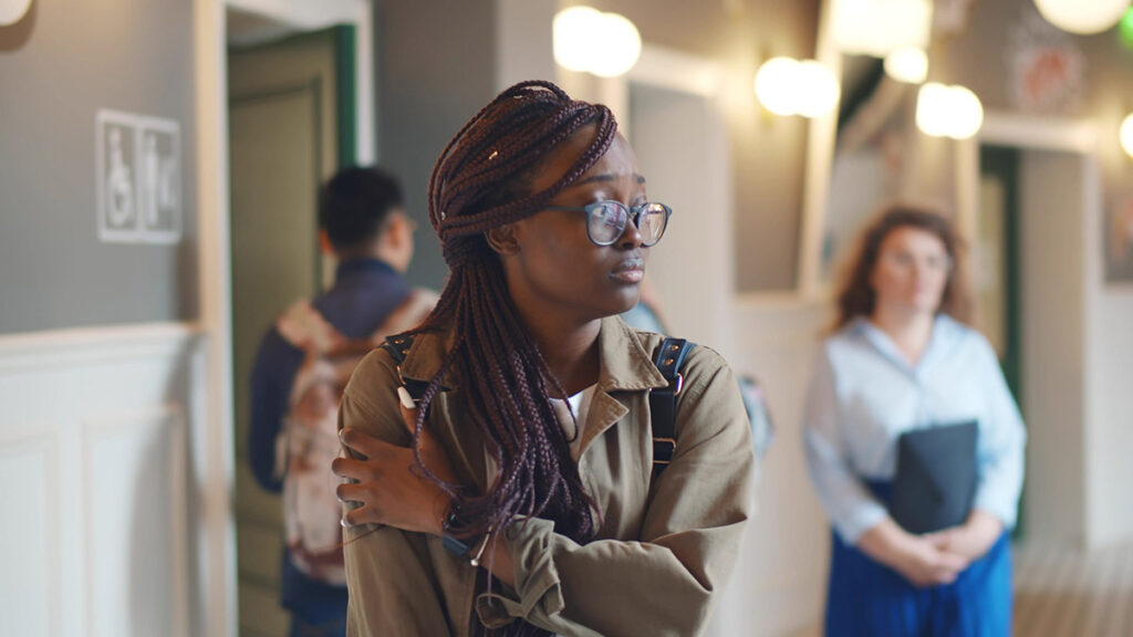 a teen girl walks the halls of her school appearing to be uncomfortable and wondering what the difference is between nervousness vs. anxiety