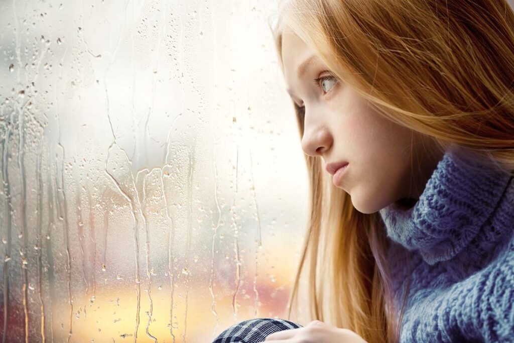 a teen girl looks out the window and displaying symptoms of depression in girls