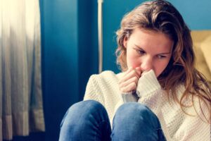 a young woman sits with her knees towards her chest looking down at the floor while thinking about the link between diet and depression