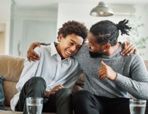 a father hugs his son while they sit together on a couch showing an example of a strong support system