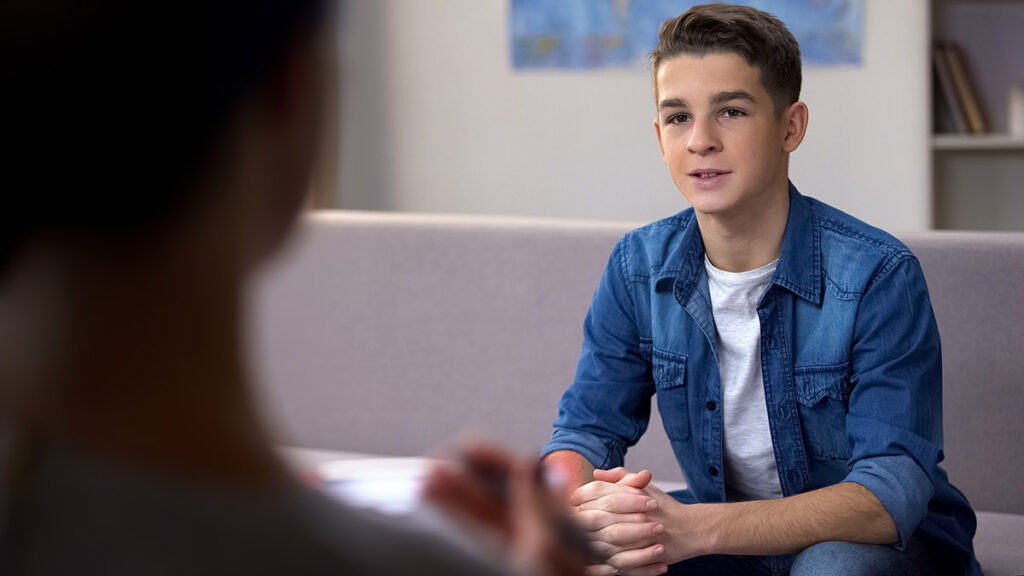 a teen boy sits on a couch and listens to his therapist explain the benefits of residential treatment for mental health