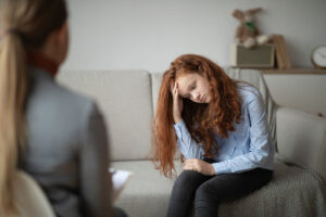 young girl sits on the couch appearing to be distraught and talks to therapist about the connection between depression and self harm