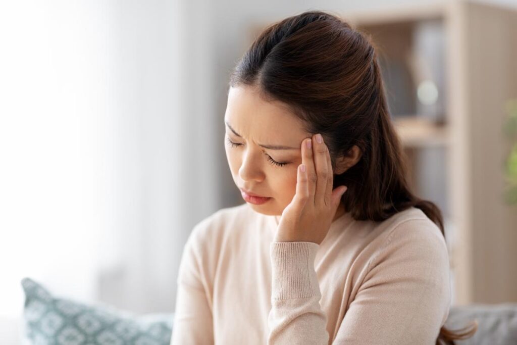 teen girl sits on a couch and holds her hand to her head in pain after realizing the connection between trauma and the brain