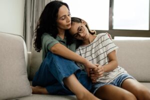 a mother holds and hugs her child on their couch while learning about how to support a loved one with depression