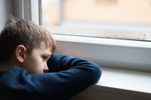 a child puts their head sadly on a windowsill, persistent sadness is one of the signs of depression in children
