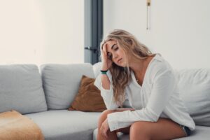 teenage girl seated on couch in brightly lit room looking concerned as she rests her head in her hand and contemplates an anxiety treatment program.