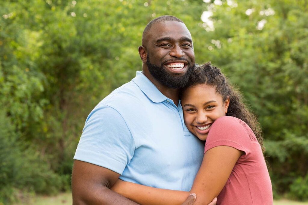 smiling father hugging his teenage daughter and asking, "Can I visit my teen during their treatment program?"