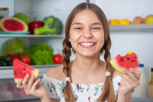 teenage girl smiling ass he is surrounded by nutritious fruits and vegetables as a testament to the role of nutrition in teen mental health