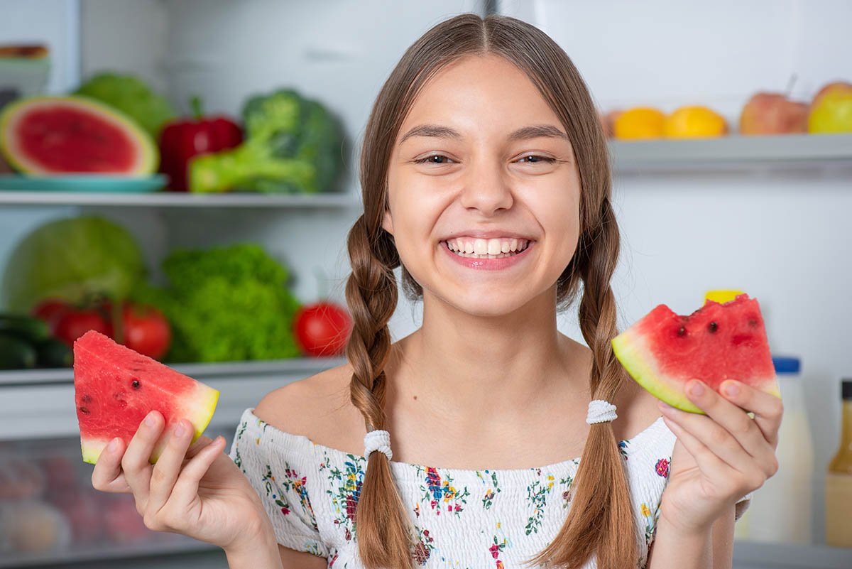 teenage girl smiling ass he is surrounded by nutritious fruits and vegetables as a testament to the role of nutrition in teen mental health