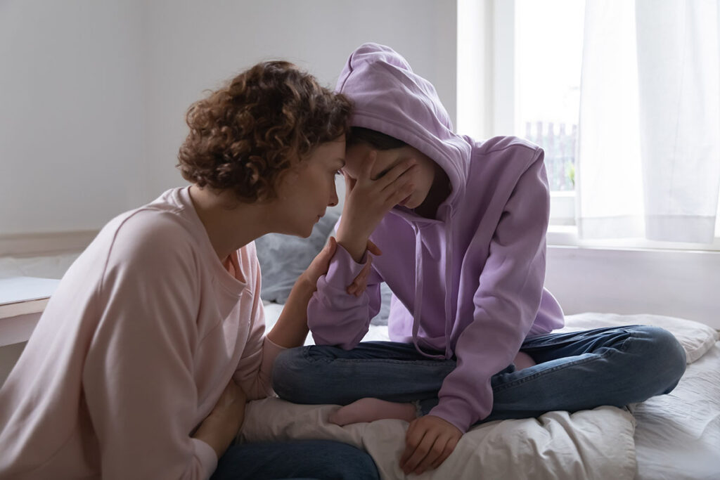 mother consoling distruaght teenage daughter in her bedroom while struggling with how to tell if my child is depressed