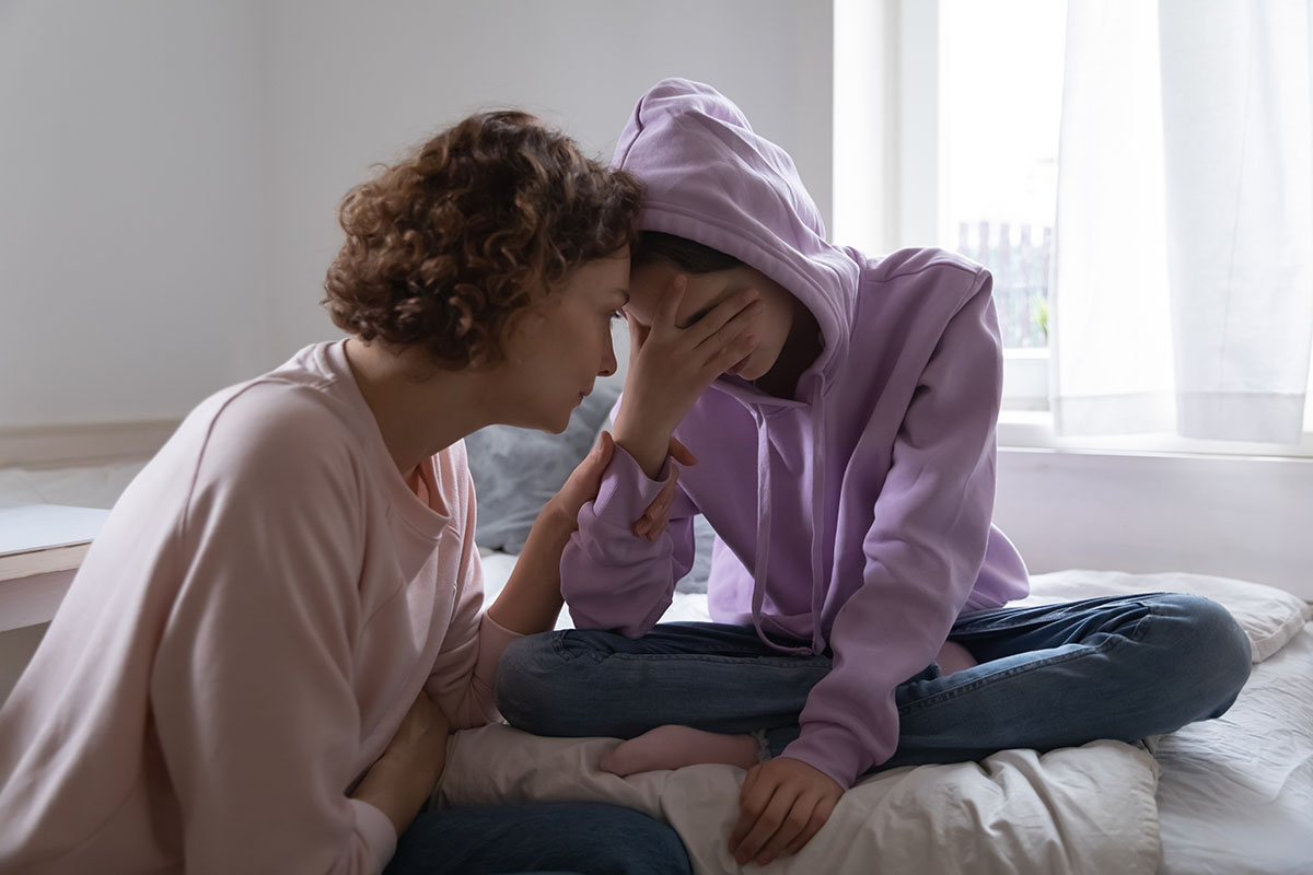 mother consoling distruaght teenage daughter in her bedroom while struggling with how to tell if my child is depressed