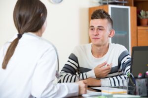 A teenage boy talks with a therapist across a desk in an office setting, appearing engaged and comfortable in conversation.