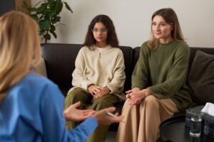 A therapist speaks with a mother and teenage daughter sitting together on a couch during a family counseling session.